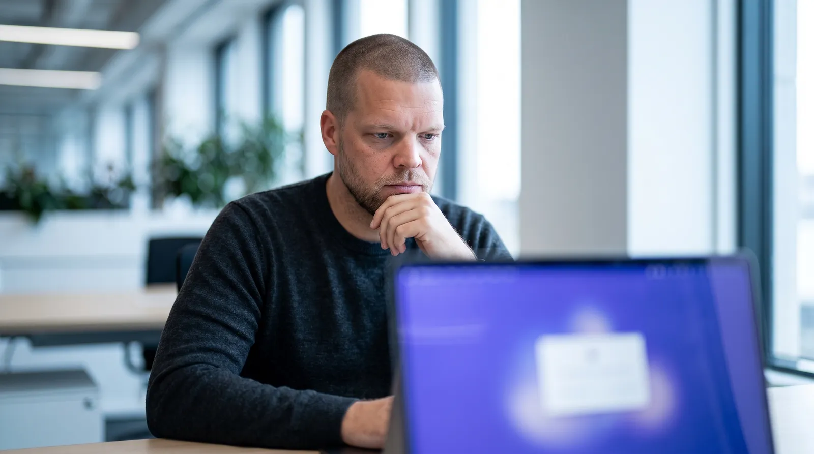 Mike Moore, founder of Strategic AI Architects, at his desk looking at a laptop screen that shows an AI agent connector settings panel next to a CRM window with a client health plan record
